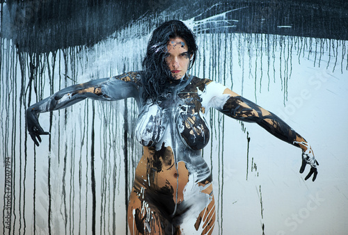 naked sensual woman with outstretched arms full of feeling, emotion in black color painted in front of Studio wall with dripping paint. Decorative abstract body painting art photo