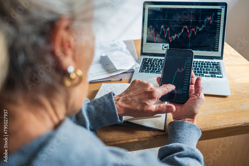 elderly retired woman senior trading on line with smartphone and laptop investment bitcoin stock market 