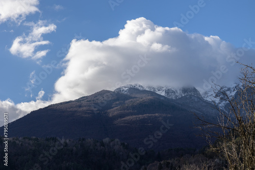 visuale in primo piano delle creste e dei boschi di una montagna nel nord est Italia, parzialmente coperti di neve e da alcune nuvole, bianche ed illuminate dal sole del mattino, in inverno photo