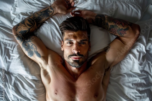 Handsome Tattooed Man Relaxing on Bed in Serene Bedroom Setting © NS