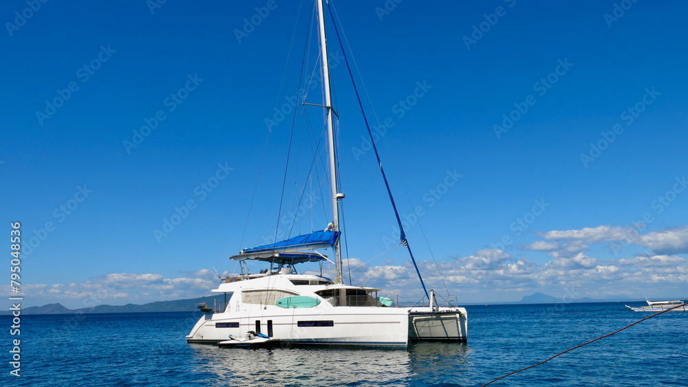 Fototapeta premium A sailing catamaran stands at sea. A catamaran with a folded sail stands in a parking lot on the open sea.