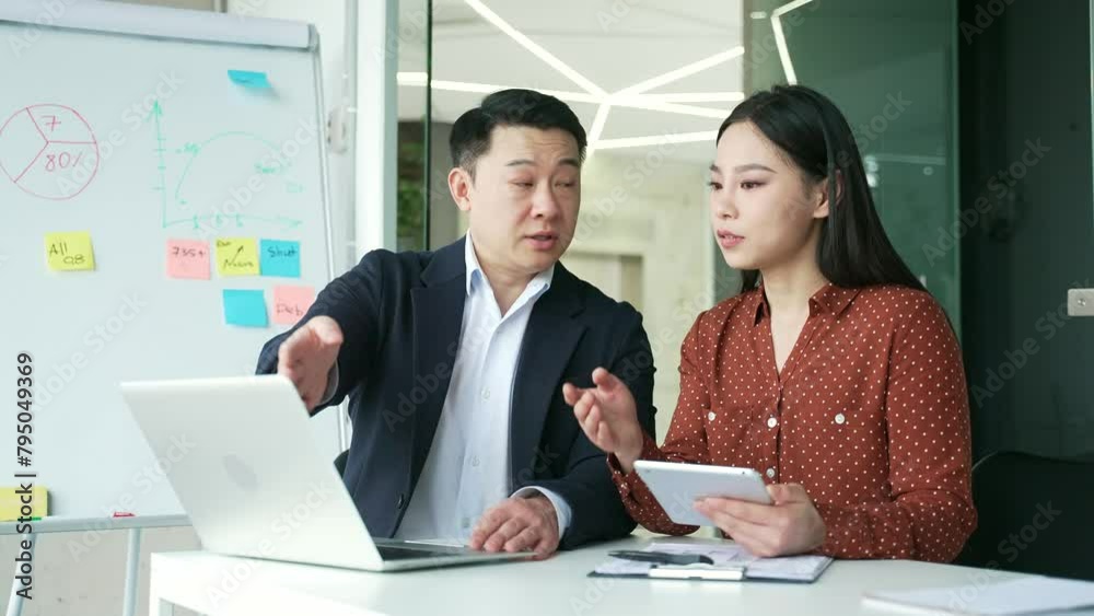 Asian boss consult young female worker at workplace in business office. Male manager advises, talking to an employee about a development project. Executive explains work issues using laptop computer Asian boss consult young female worker at workplace in business office. Male manager advises, talking to an employee about a development project. Executive explains work issues using laptop computer