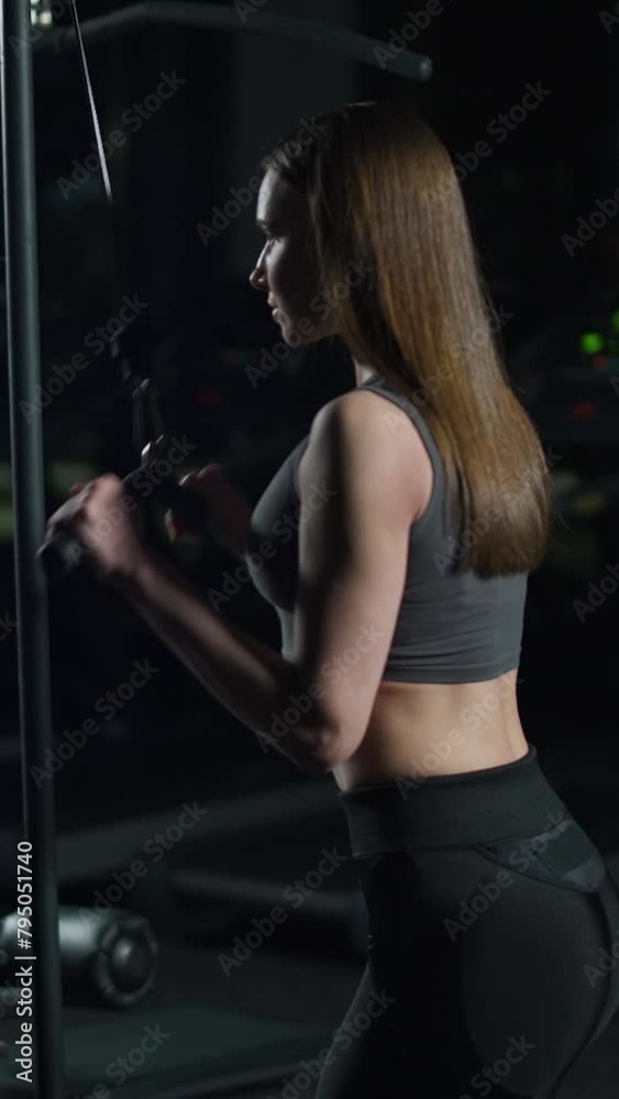 Sporty woman in the gym lifting blocks on gym machine, strength training on block device and gym equipment, night training, vertical video. Sporty woman in the gym lifting blocks on gym machine, strength training on block device and gym equipment, night training, vertical video.