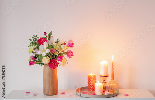  flowers  in vase and burning candles on shelf  on background wall