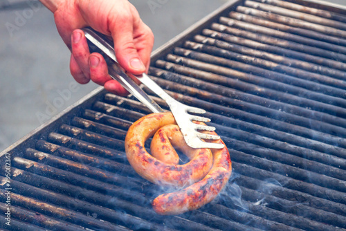 Male hand with a fork touching sausage on the grill
