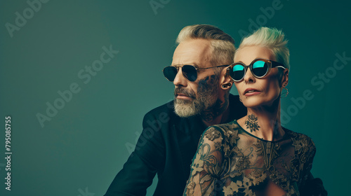 A mature couple with sunglasses and tattoos in the style of haute couture, teal colors, golden details. The man has short gray hair and a stubble beard. The woman is older wearing a lace dress