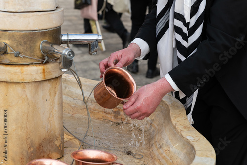 Closeup of a man using a copper cup to ritually wash his hands before prayer at the Western Wall in Jerusalem, Israel. photo