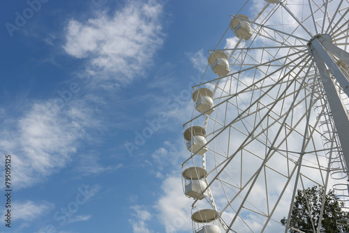 A large, tall white Ferris wheel against a blue sky background. Happy feelings from the summer holidays