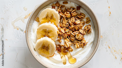 A bowl of creamy Greek yogurt topped with granola clusters, sliced bananas, and honey drizzle creating an appetizing and wholesome breakfast or snack option against a minimalist white backdrop.