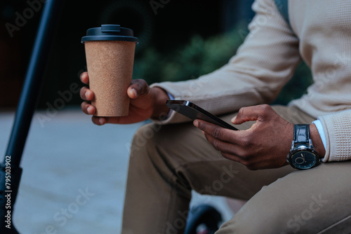 Man holding phone and coffee outdoors (ID: 795103902)