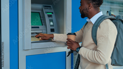Man at ATM machine with a coffee cup (ID: 795103961)