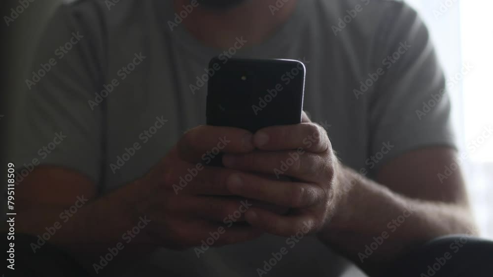 Silhouetted by light streaming through a window, a man in a dark room navigates his phone for an essential phone call. Silhouetted by light streaming through a window, a man in a dark room navigates his phone for an essential phone call.