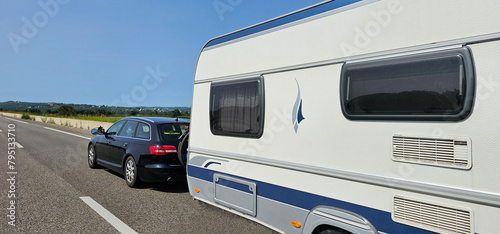 Car towing a caravan trailer on a freeway; automobile pulling a trailer camper on a quiet road in Spain on a sunny day.