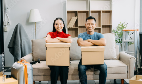 Young couple with big boxes moving into a new house, new apartment for couple, young asian man and woman helping to lift boxes on sofa for the new home.