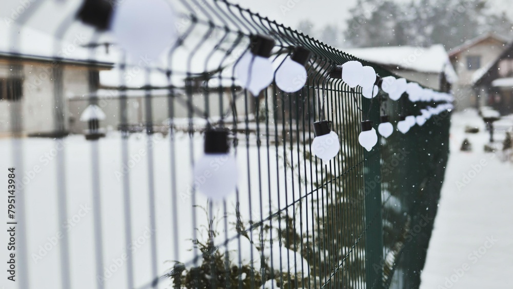 A white garland of bulbs on a fence in winter.