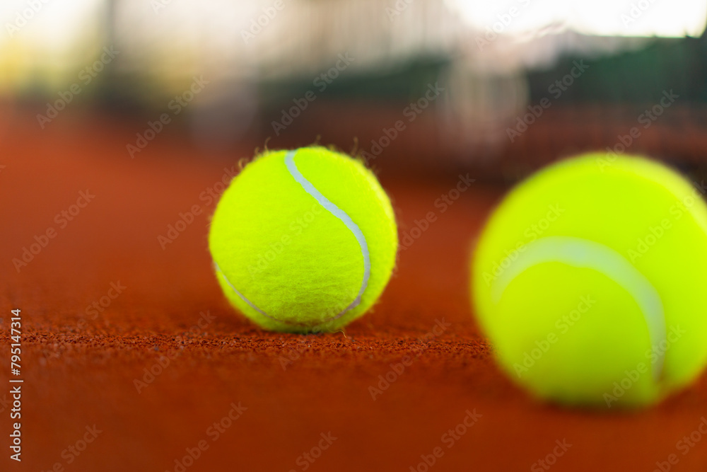 tennis balls on orange clay court with blurred net in background