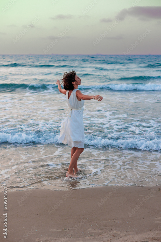 happy young girl in a white summer dress walks along the beach at sunset.