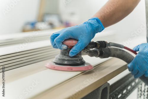 close-up hands of worker with gloves using electric sander in workshop. Joiner sanding wooden board on table. Carpentery work. High quality photo