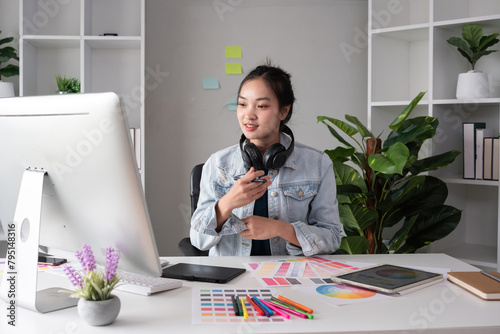 Female designer wearing headphones listening to music while doing graphic design work Choose colors for working with the computer at the table.
