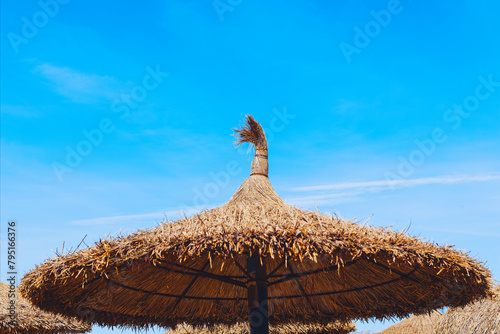 Straw umbrella on the beach with blue sky background. Exotic parasol made by sedge
