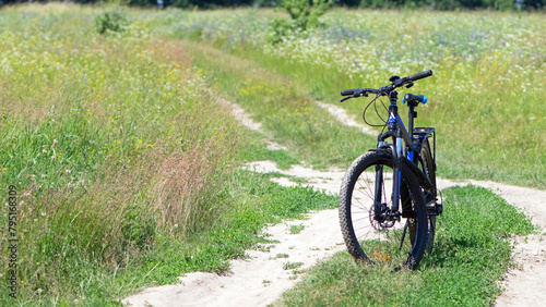 bike stands on the road in the field. A mountain bike stands on a field path with green grass. Mountain bike, blooming summer field, meadow flowers, sunny day. ride a bike. outdoor activities.