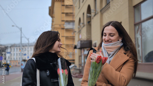Two young girls, friends with flowers in their hands, walk along a city street