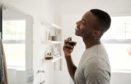 Smiling young African man spraying on cologne in his bathroom