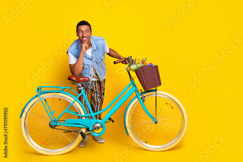 Full size photo of cheerful man dressed denim vest over t-shirt hold cycle look at sale empty space isolated on yellow color background