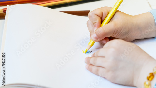 Close-up of a child's hands drawing with colored pencils. Children's creativity and development, fine motor skills, learning to write and draw.