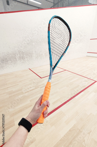 squash racket in the hands of an athlete on the background of a squash court