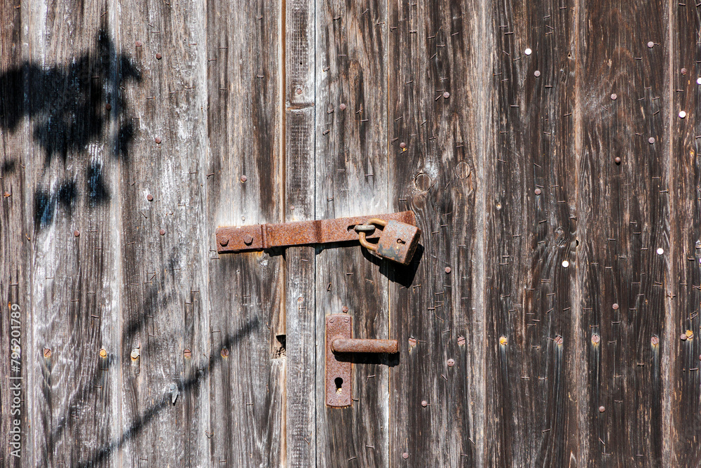 A rusty old padlock on a brown double-leaf wooden door A rusty old padlock on a brown double-leaf wooden door