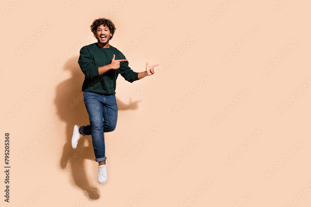 Full body portrait of nice young man jump point fingers empty space wear sweater isolated on beige color background Full body portrait of nice young man jump point fingers empty space wear sweater isolated on beige color background