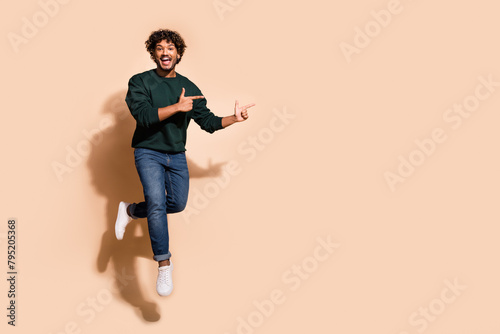 Full body portrait of nice young man jump point fingers empty space wear sweater isolated on beige color background
