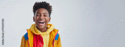 A young boy wearing a yellow jacket and a red and blue hoodie is smiling. secondary school pupil being happy and smiling  bright clothes  white background