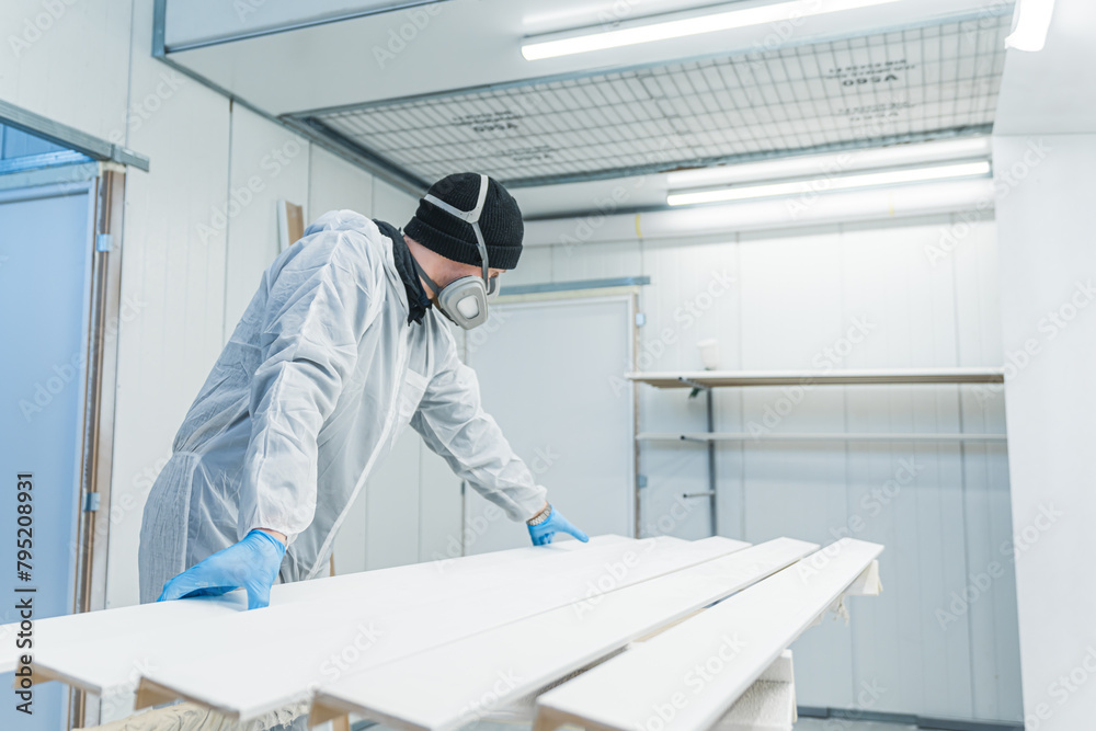 a carpenter with uniform and mask in the process of spraying wooden pieces, workshop. High quality photo