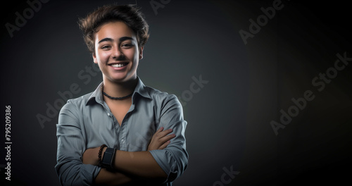 A man with a black shirt and a black background. He is smiling and has his arms crossed. student with happy expression and crossed arms