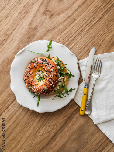 Bagel sandwich with tuna eggs salad and arugula - delicious breakfast, snack on a wooden background, top view