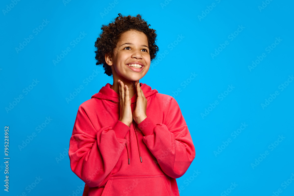 Happiness and excitement moment, African-American girl in pink hoodies expressing happiness and joy against blue studio background. Concept of childhood, human emotions, lifestyle