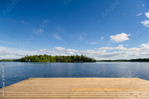 Fototapeta Naklejka Na Ścianę i Meble -  A spacious wooden dock gracefully stretches into the serene waters of a tranquil lake in Muskoka, Ontario, Canada.