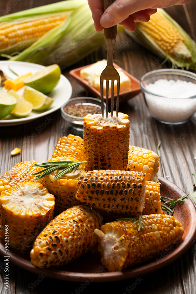 Female taking grilled sweet corn piece from plate with the fork