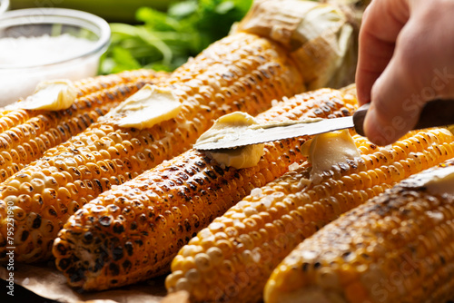 Grilled sweetcorn cobs on the table being seasoned with butter closeup low angle view