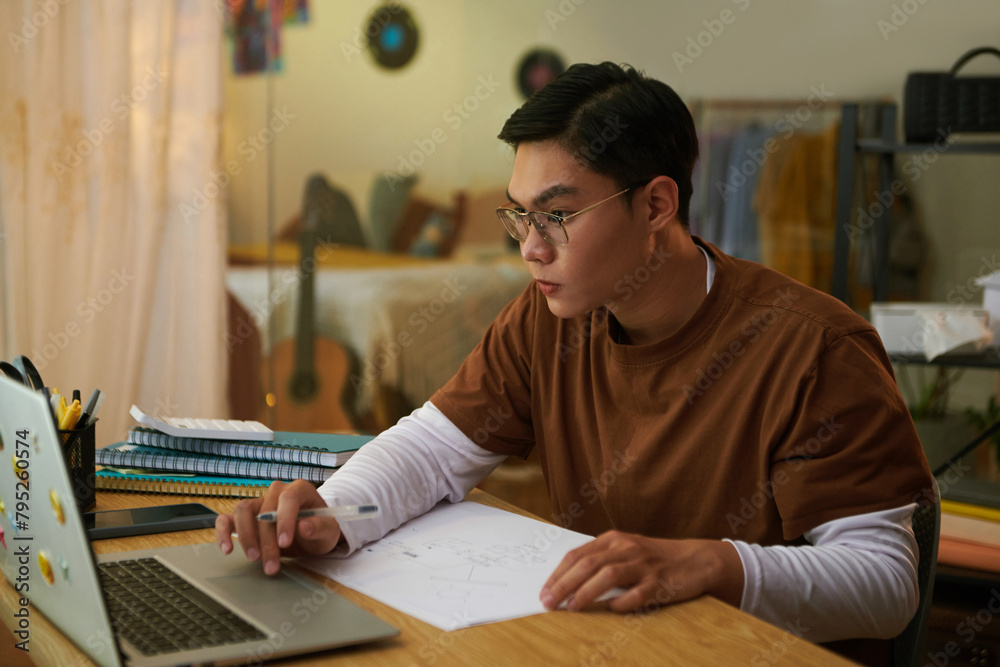 College student watching educational video when drawing wireframe of his fist mobile app