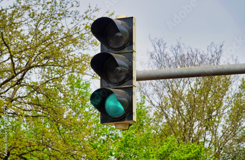 Green lit traffic light high up with trees in the background photo