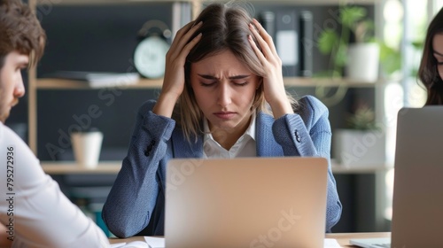 Stressed young american woman holding head in hands and feeling demotivated while sitting at her home office and working remotely on laptop. photo