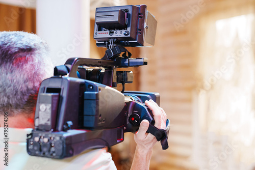 A gray-haired man holds a large professional video camera in his hands.