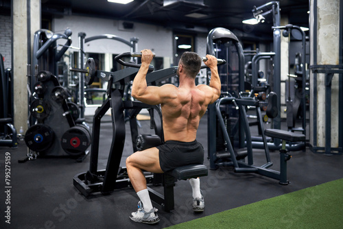 Attractive muscular man doing exercise with training apparatus in sports gym. Back view of strong unrecognizable male athlete with bare torso, building muscles indoors. Sport, bodybuilding concept.