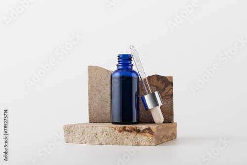 Blue glass serum bottle for organic cosmetic on natural stone podium