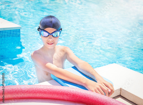 Child (boy) in cap, sport goggles ready to learns professional swimming with pool board, swim noodles. Kid enjoying water in swimming pool. Healthy lifestyle. Copy space. Empty space.