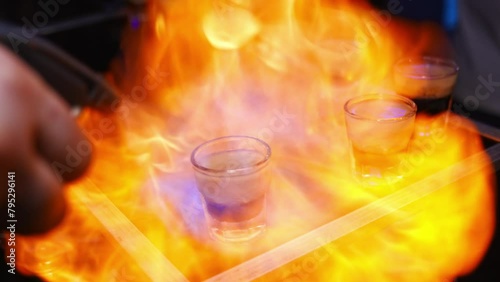 The bartender sets fire to cocktails in stacks on counter. fire show