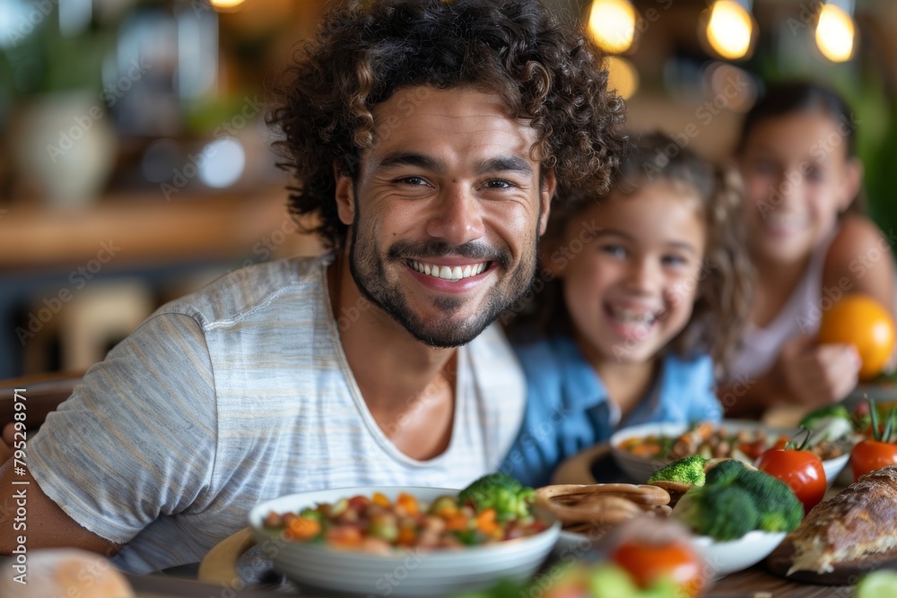 Smiling man with curly hair enjoying a meal with a child and others, focus on healthy food